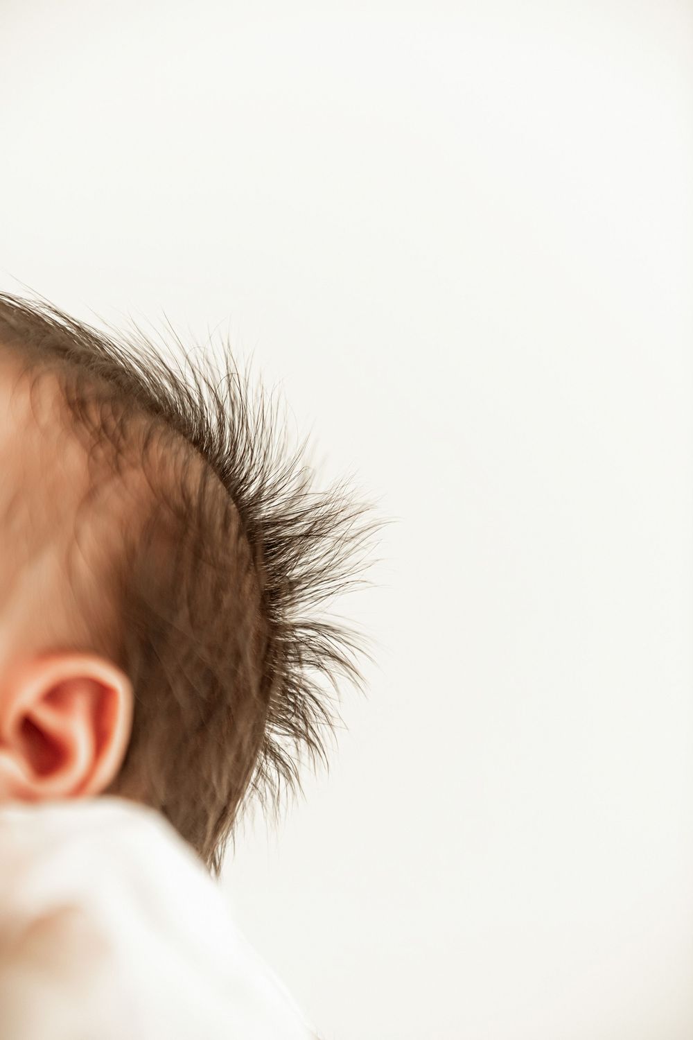 Close-up side view of a baby's spiky hair and ear against white background.