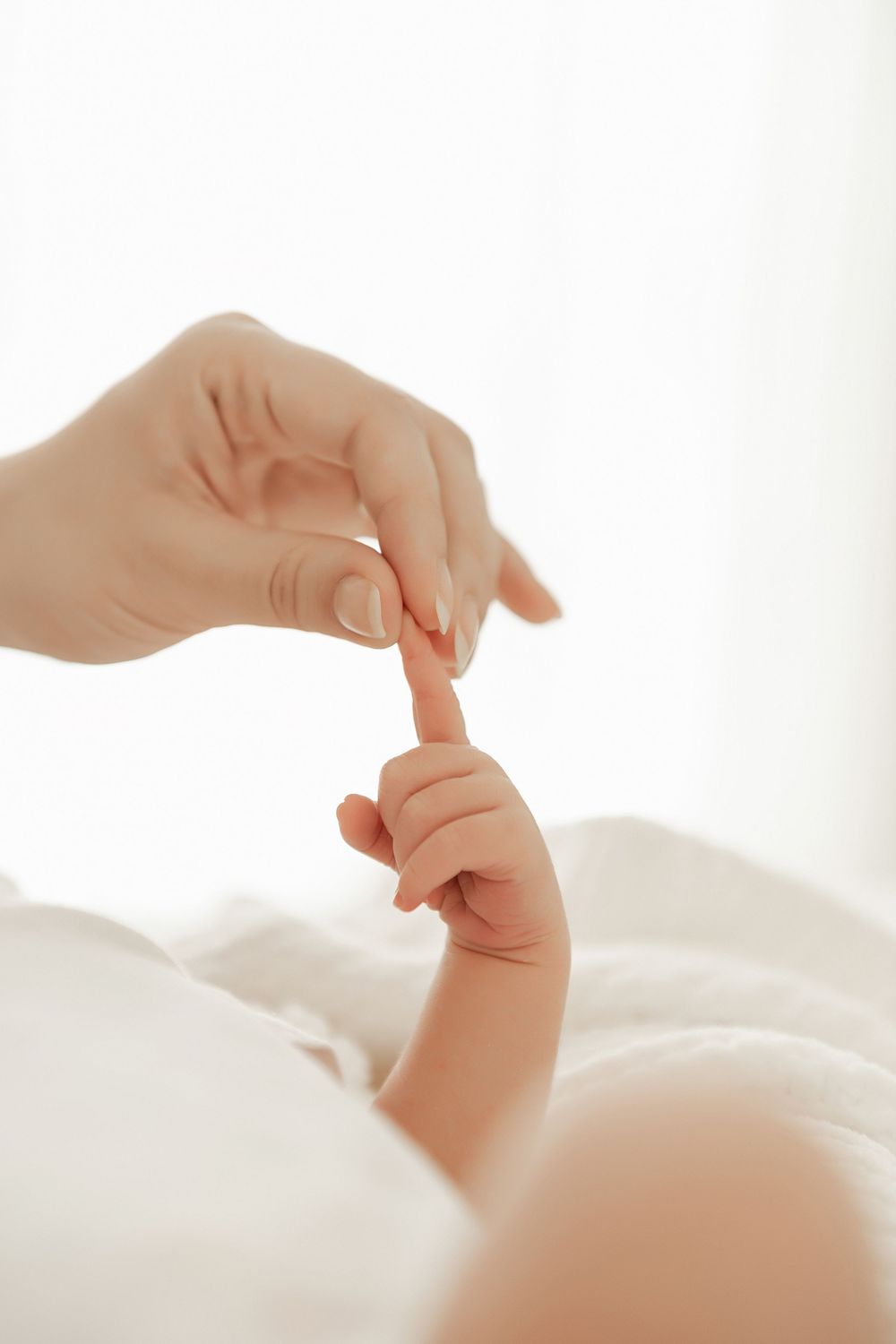 Small baby hand reaching up to touch adult finger against bright white background.