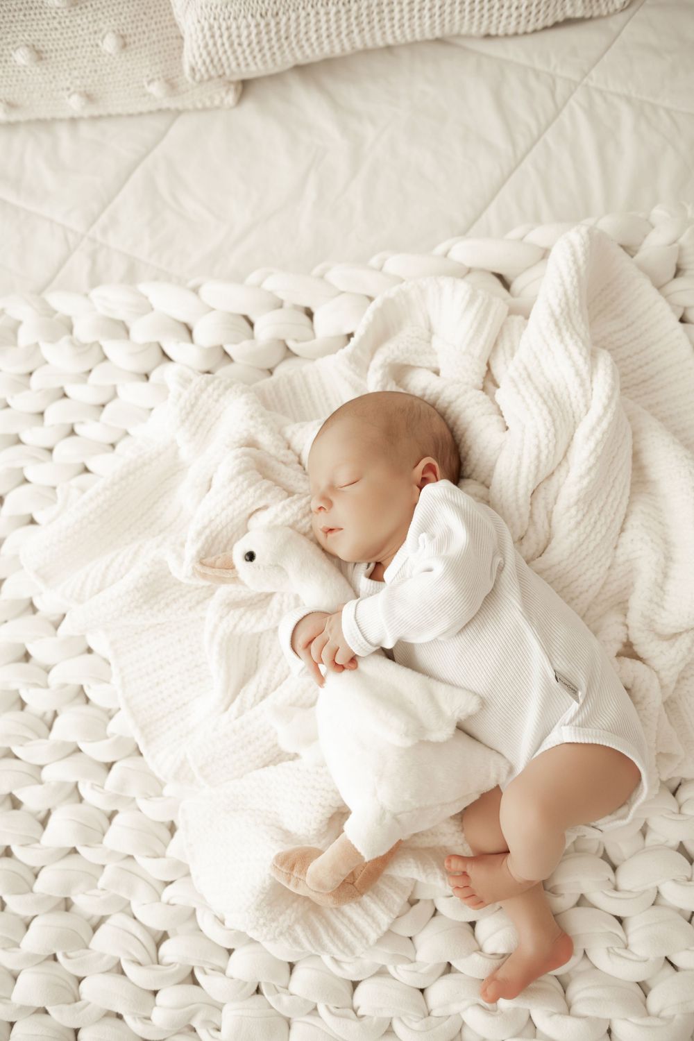 Sleeping baby in white clothing lies on plush chunky knit blanket in peaceful nursery setting.