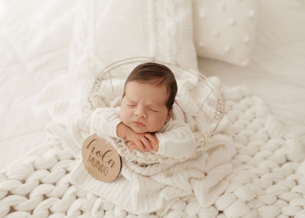 A sleeping newborn baby wrapped in soft white blankets rests peacefully on textured bedding.