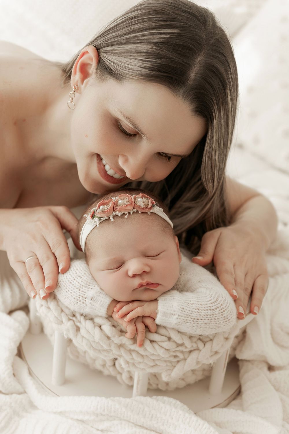 A tender moment captured in soft white tones as mother and newborn share intimate cuddles during a professional photo session.
