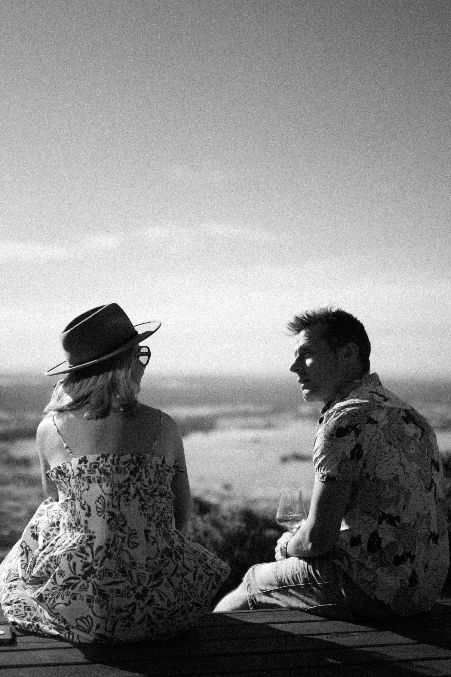 Black and white photo of a couple sitting on a deck overlooking a vast landscape.
