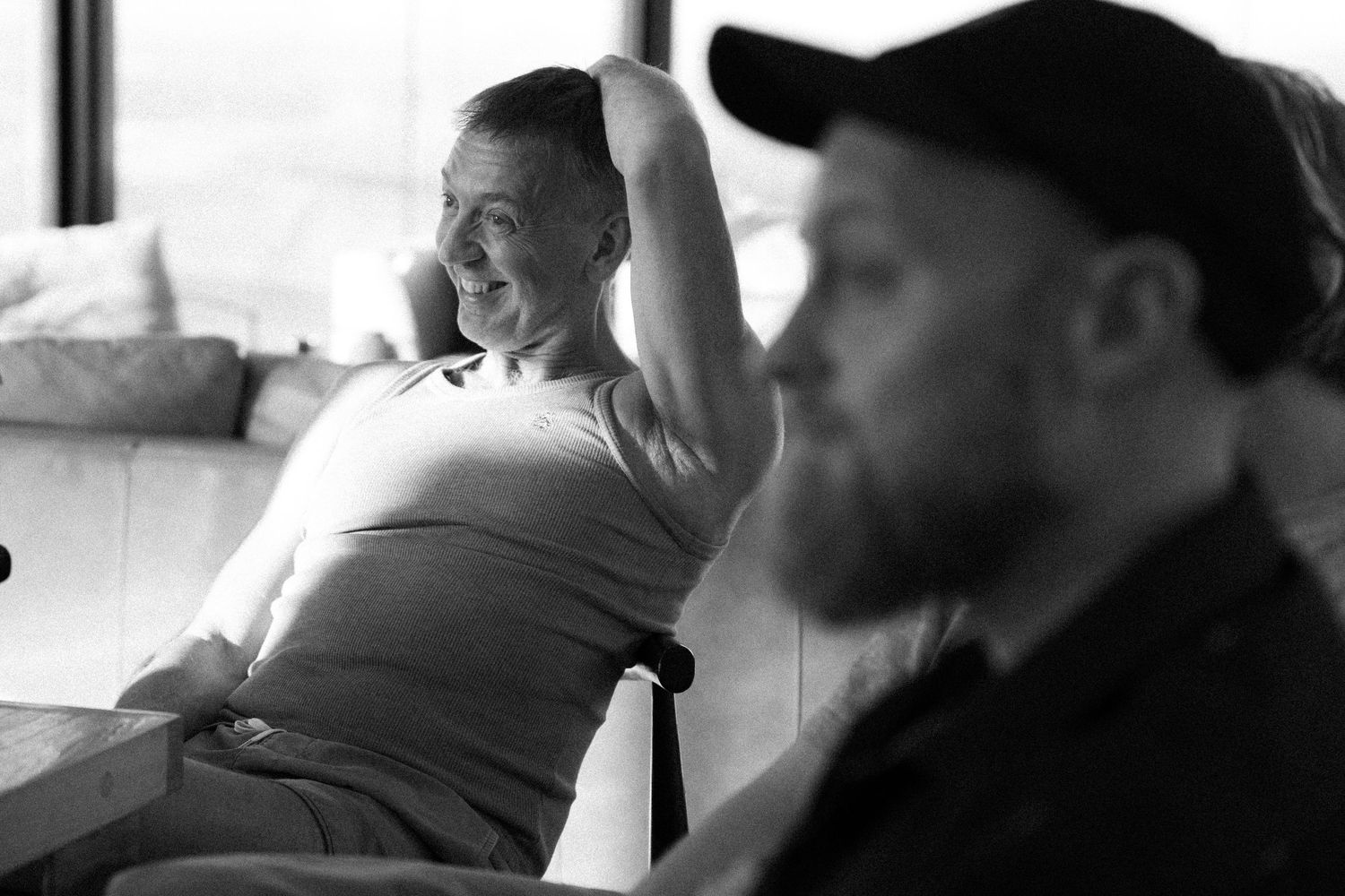 Black and white photo of two men relaxing indoors, one smiling with hands behind his head.