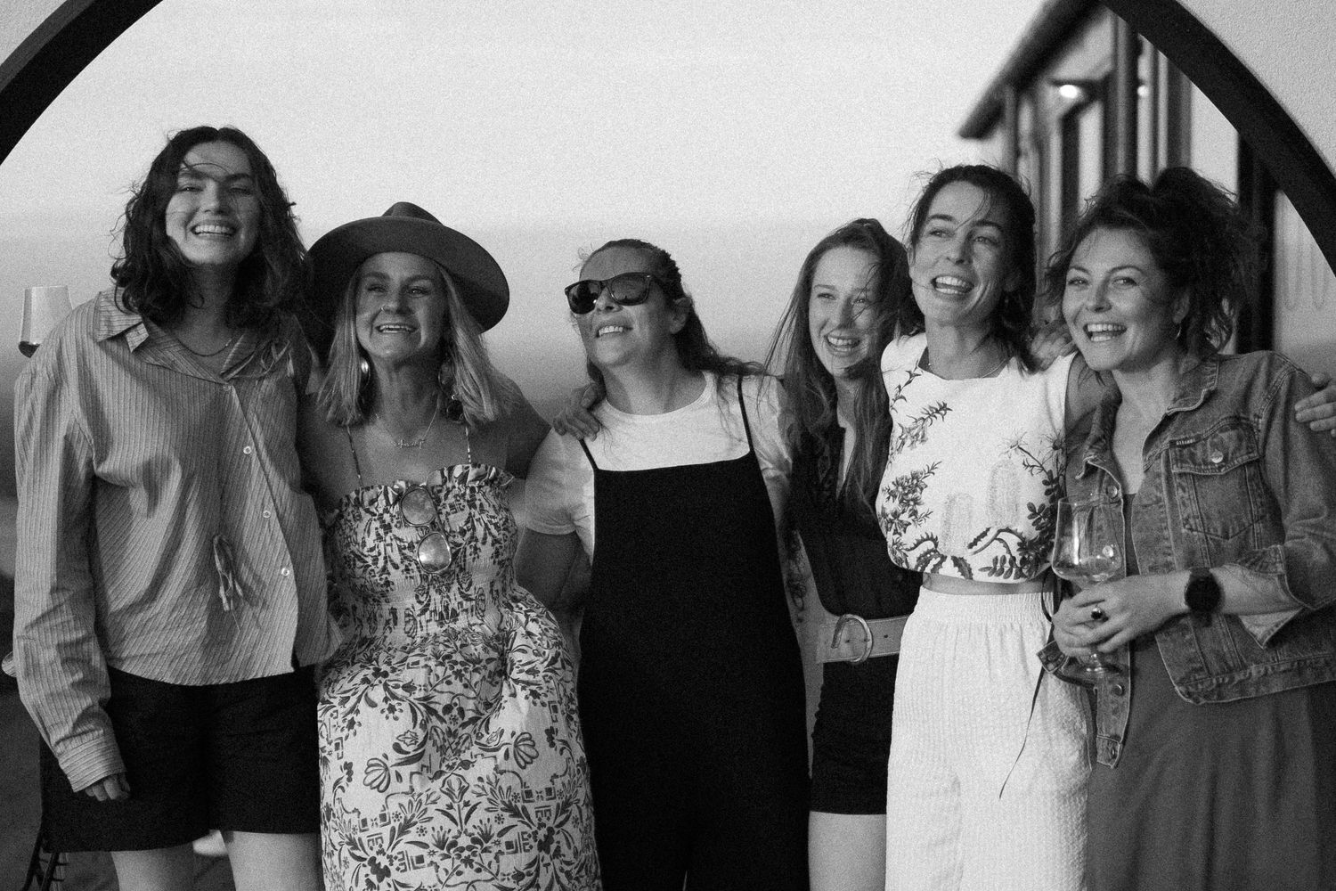 Black and white photo of six women smiling and posing together outdoors.