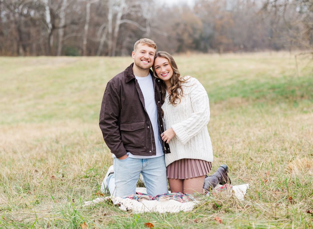 Couple sitting on blanket in field wearing coordinated fall outfits.