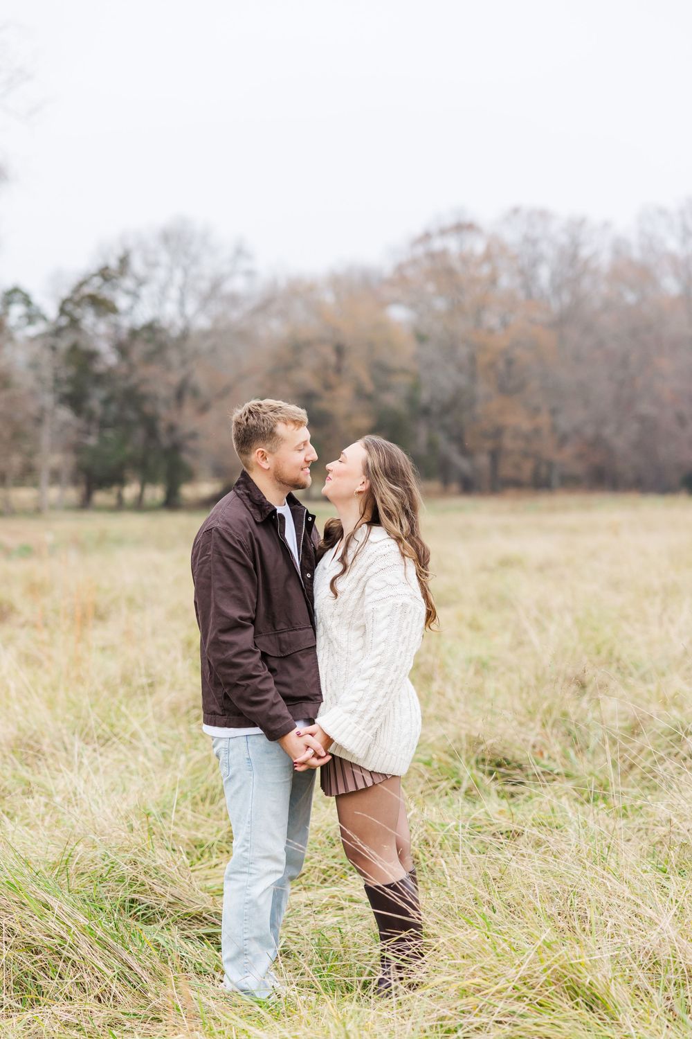 A couple holds hands while standing in tall grass during an autumn photo session.