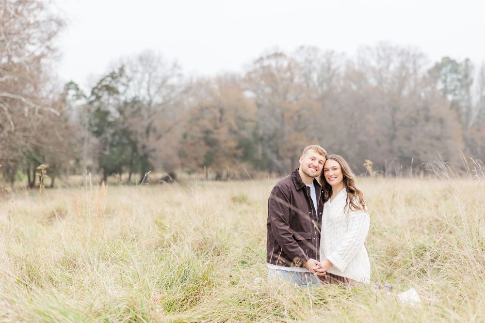 A couple shares a tender moment while sitting together in tall grass during autumn.
