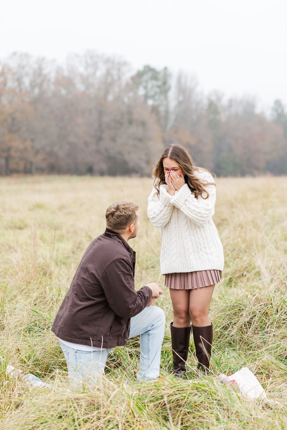 A surprise proposal moment captured in a rustic field setting.