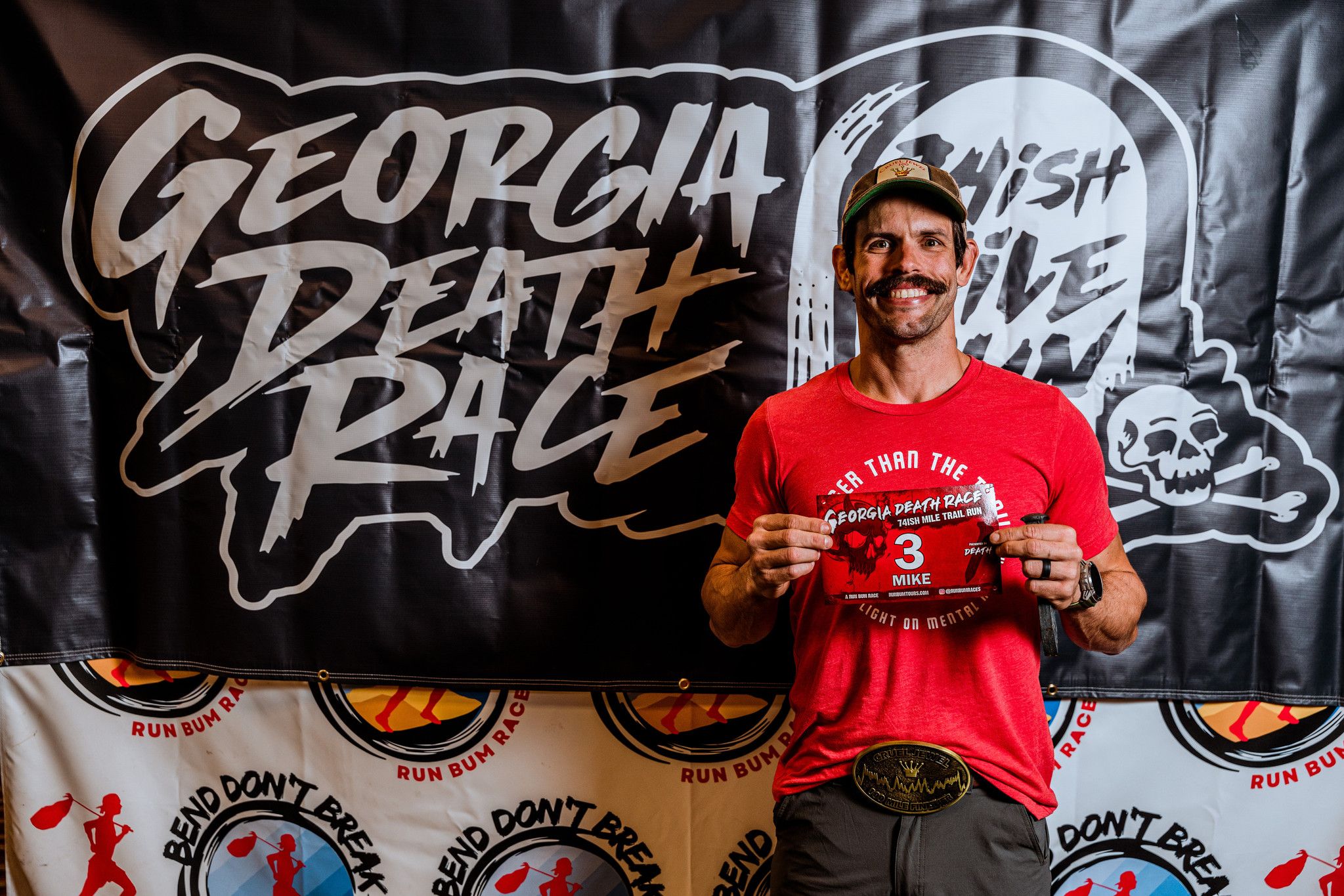 Runner displays medal in front of Georgia Death Race banner with skull design.