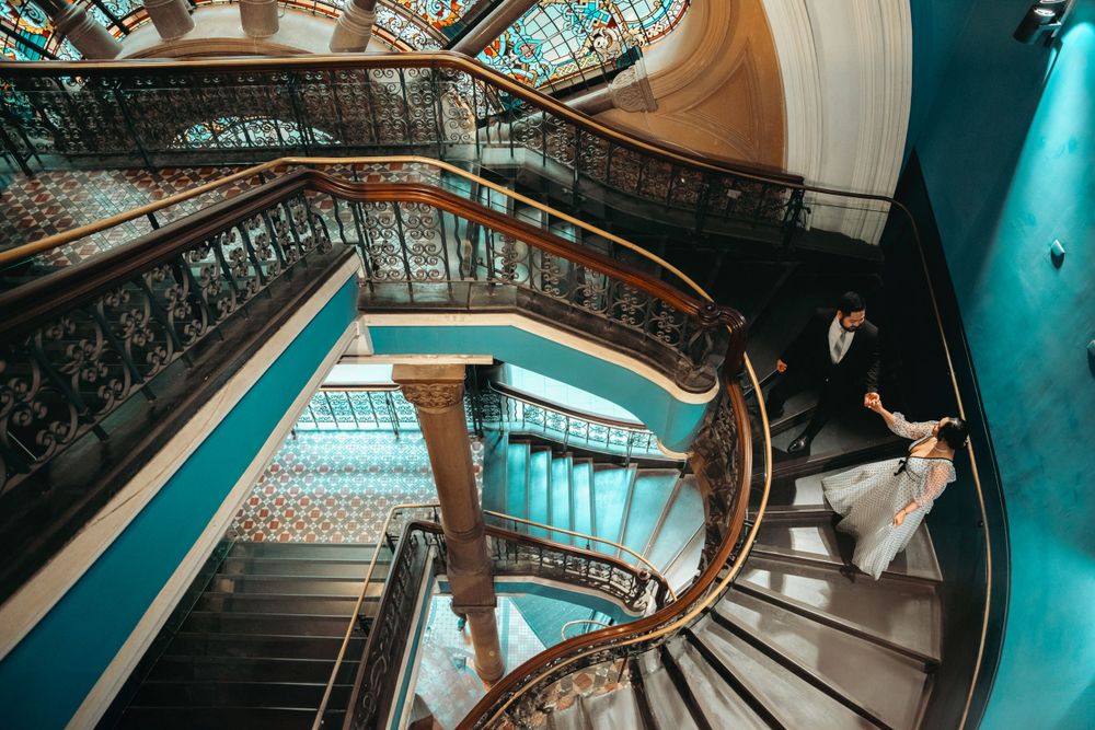 Elegant spiral staircase with ornate railings in turquoise and gold tones creates dramatic wedding photo setting.
