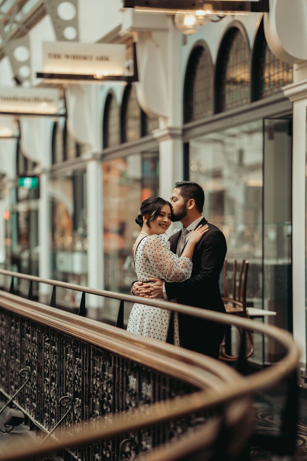 Romantic moment captured in vintage shopping arcade with arched windows and elegant architecture.
