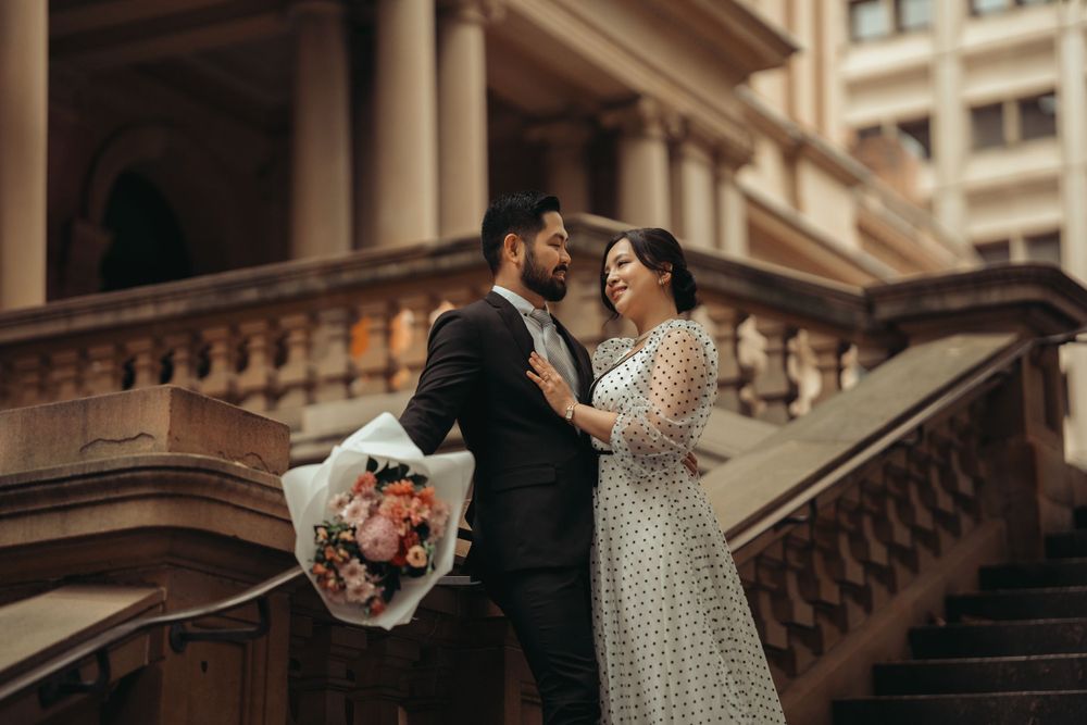 Romantic portrait on grand stone staircase with classical architecture and floral bouquet.