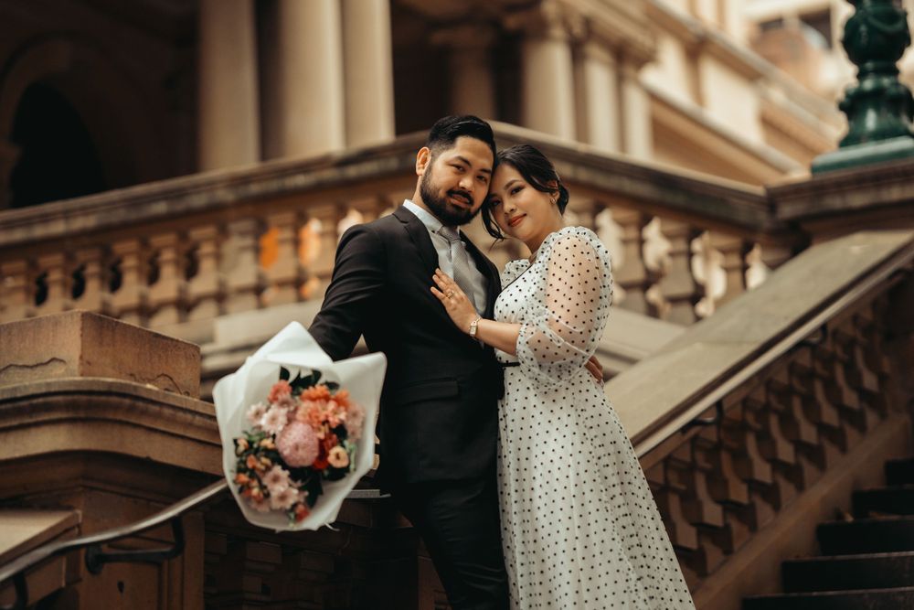 Tender moment captured on historic building steps with pink floral bouquet.