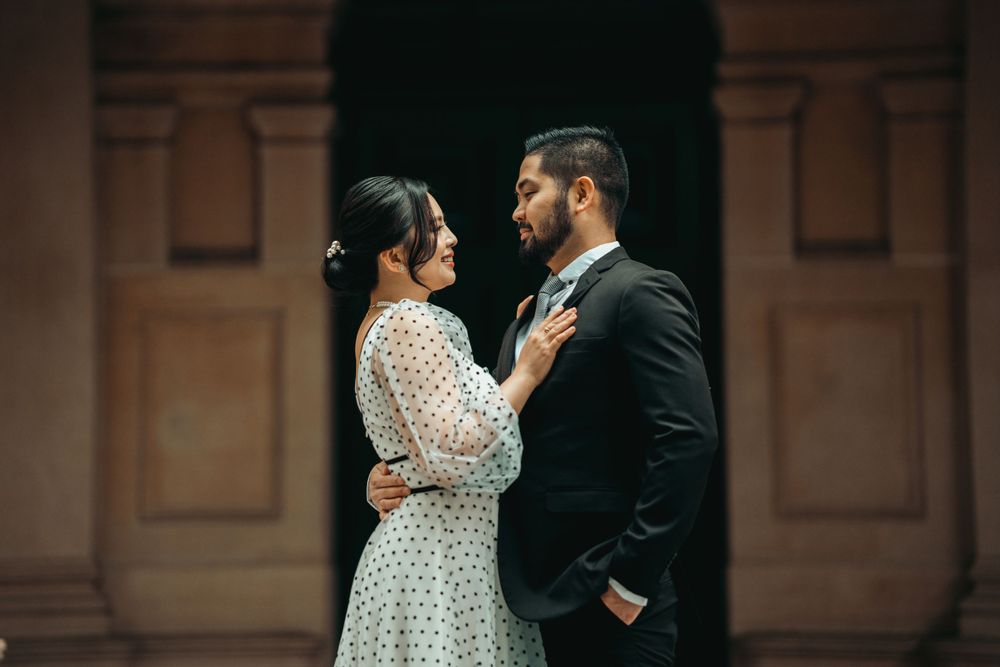 Romantic couple embraces in formal attire against an ornate architectural backdrop.