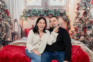 Couple sharing joyful moment on red couch with Christmas decorations behind them.