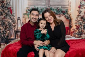Cheerful family portrait with festive Christmas decorations and red couch backdrop.