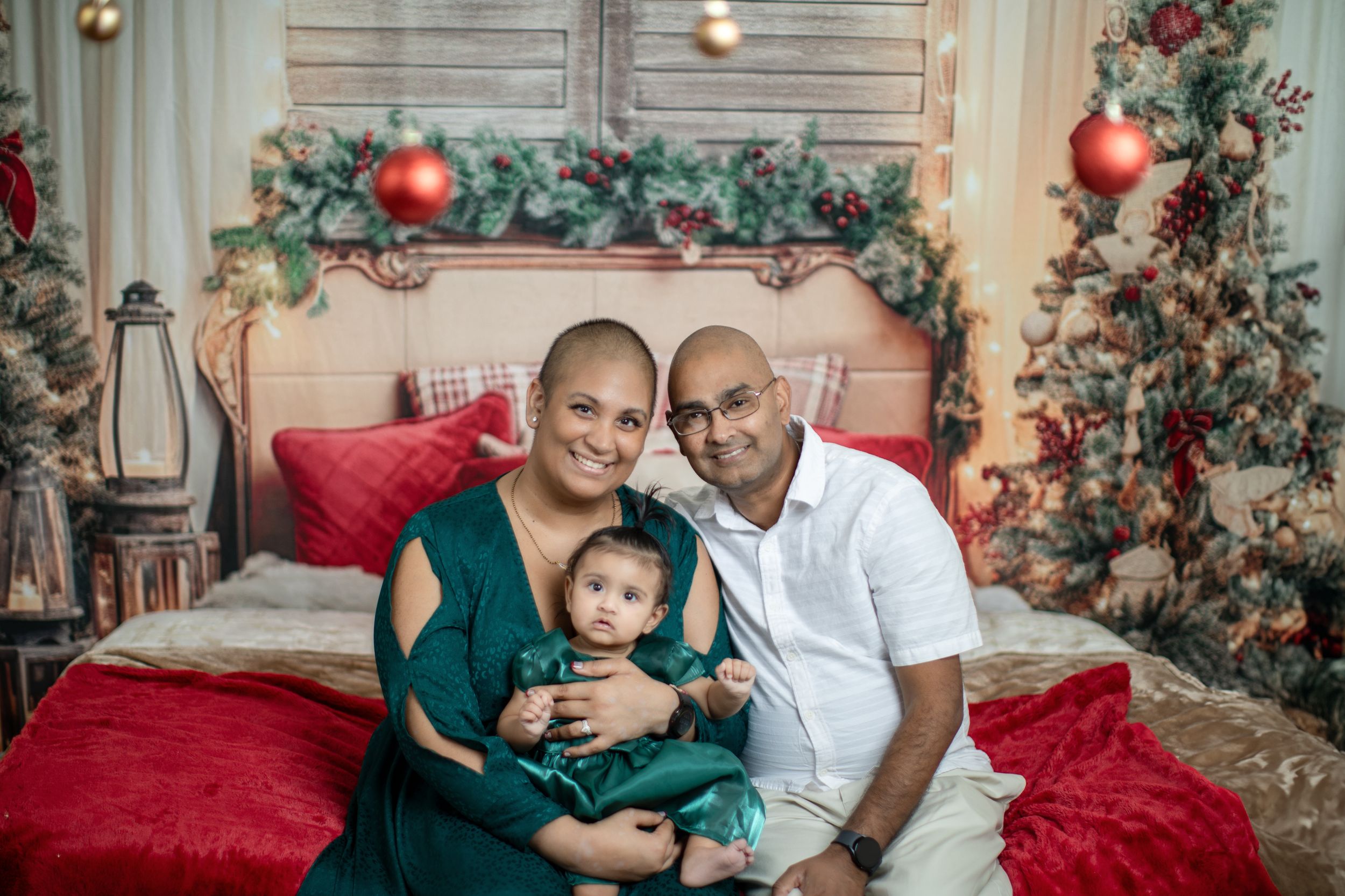 Family holiday portrait on red couch with Christmas trees and decorative garland in background.