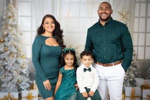 Elegant family photo with coordinated teal and white outfits by Christmas tree.
