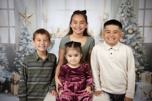 Siblings pose together in front of Christmas decor with white winter wonderland backdrop.