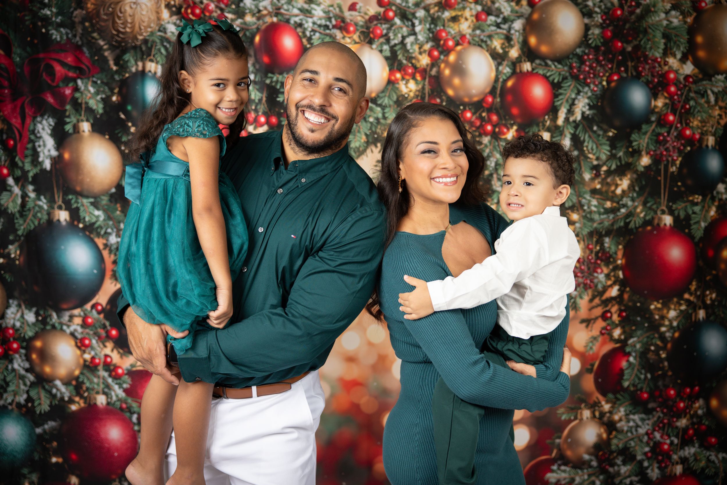 Joyful family portrait with matching teal outfits against festive Christmas backdrop.