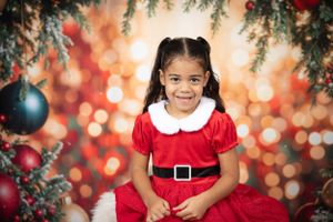 Holiday portrait in red Santa dress against warm bokeh background with ornaments.