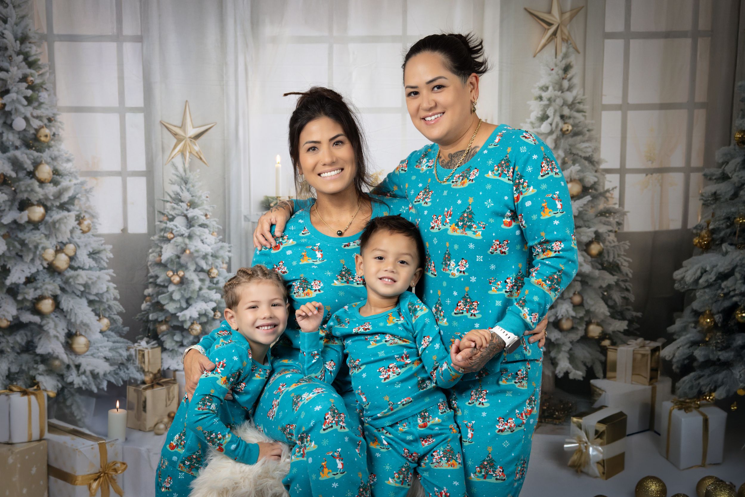 Family wearing matching blue holiday pajamas pose in front of decorated Christmas tree.