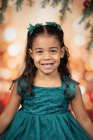 Holiday portrait with teal dress and matching hair bows against warm bokeh lights.