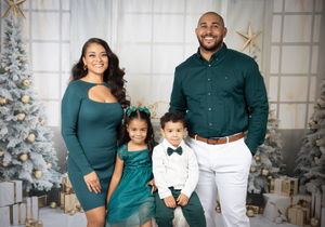 Family dressed in coordinating teal and white outfits pose by Christmas tree.