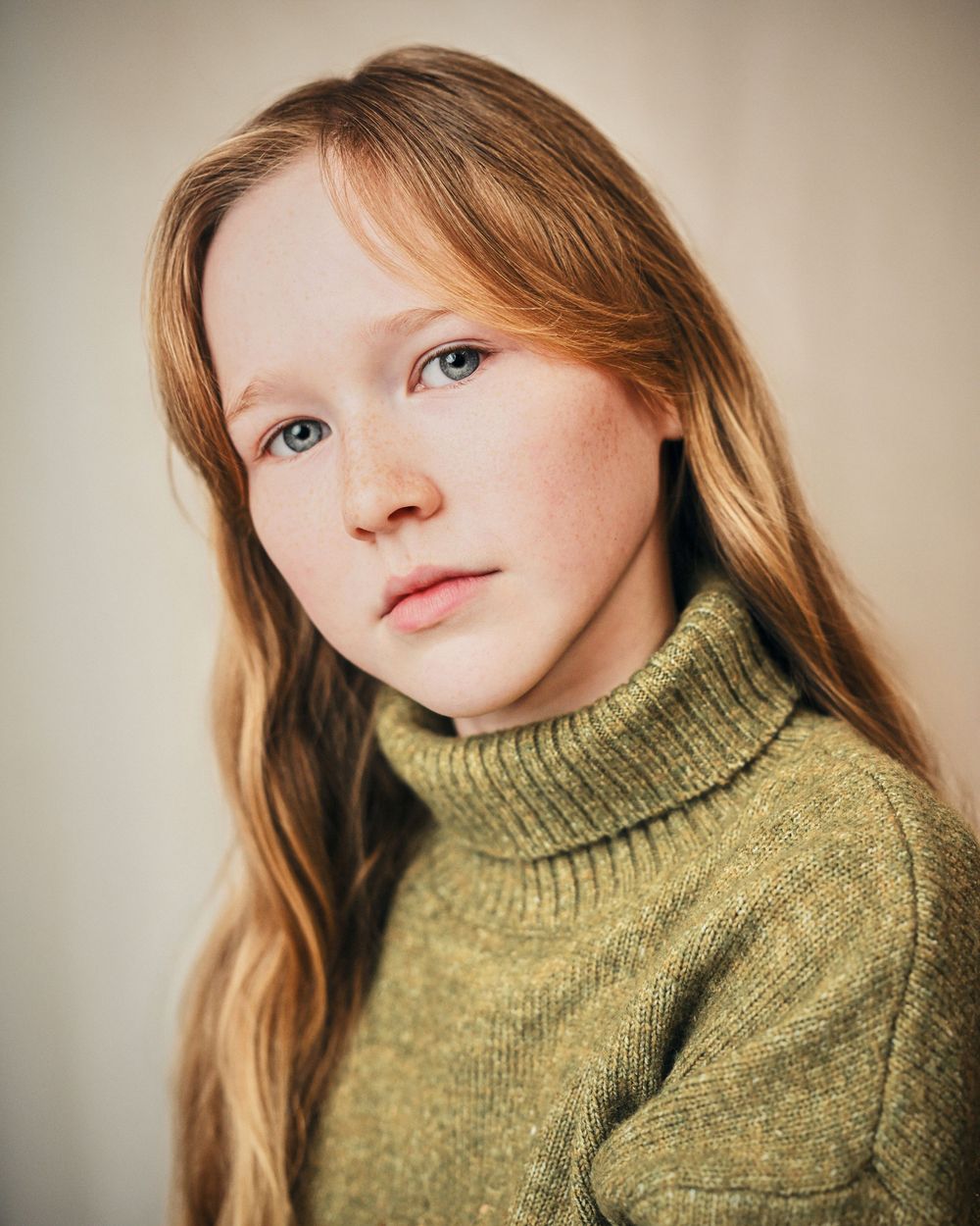 Young girl with red hair, freckles, and blue eyes wearing a green turtleneck sweater in a portrait photo.