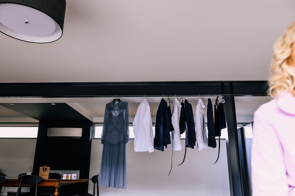 Formal clothing and dress shirts hanging from black ceiling rack in a minimalist interior.