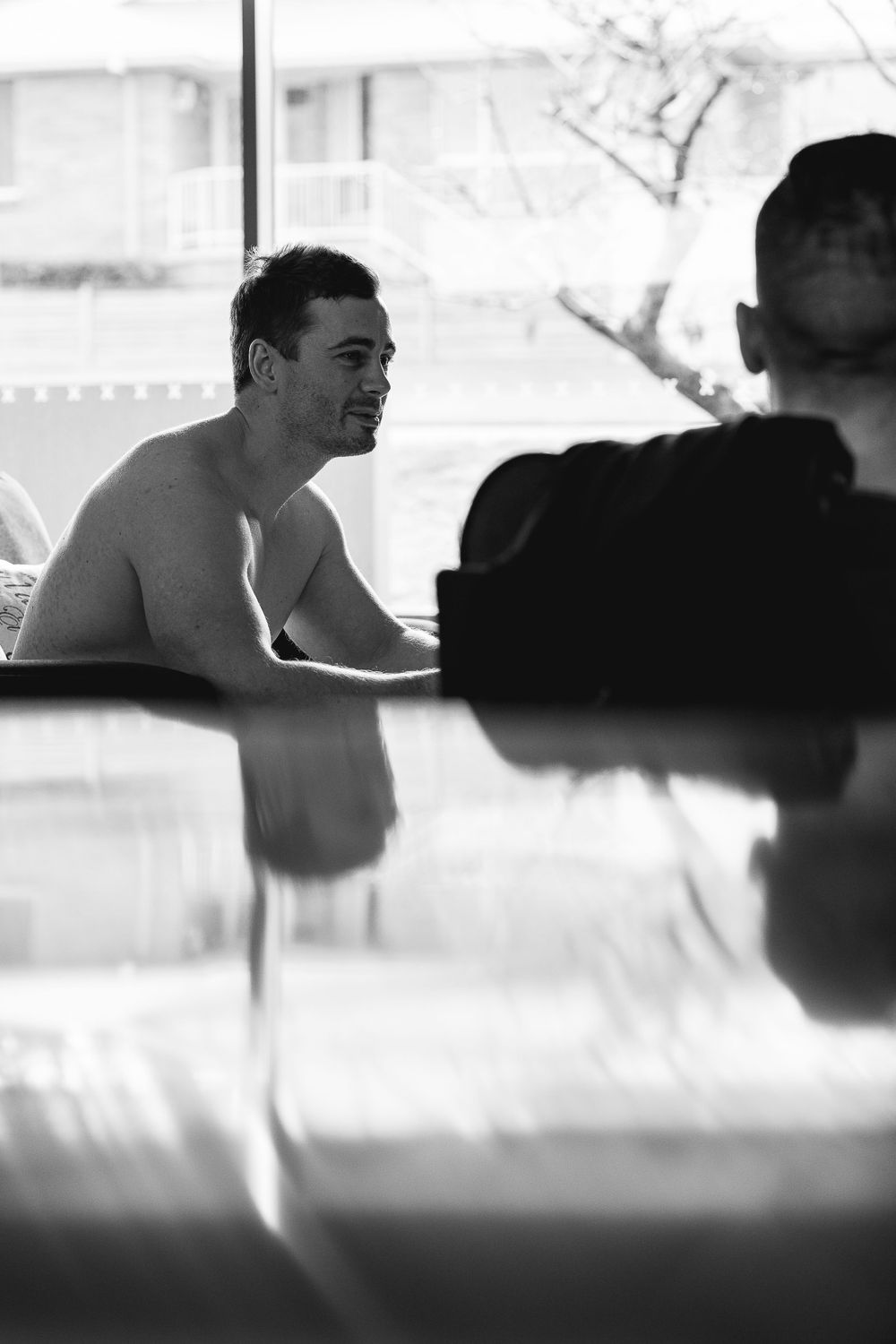 Black and white candid photograph of people conversing by a window.