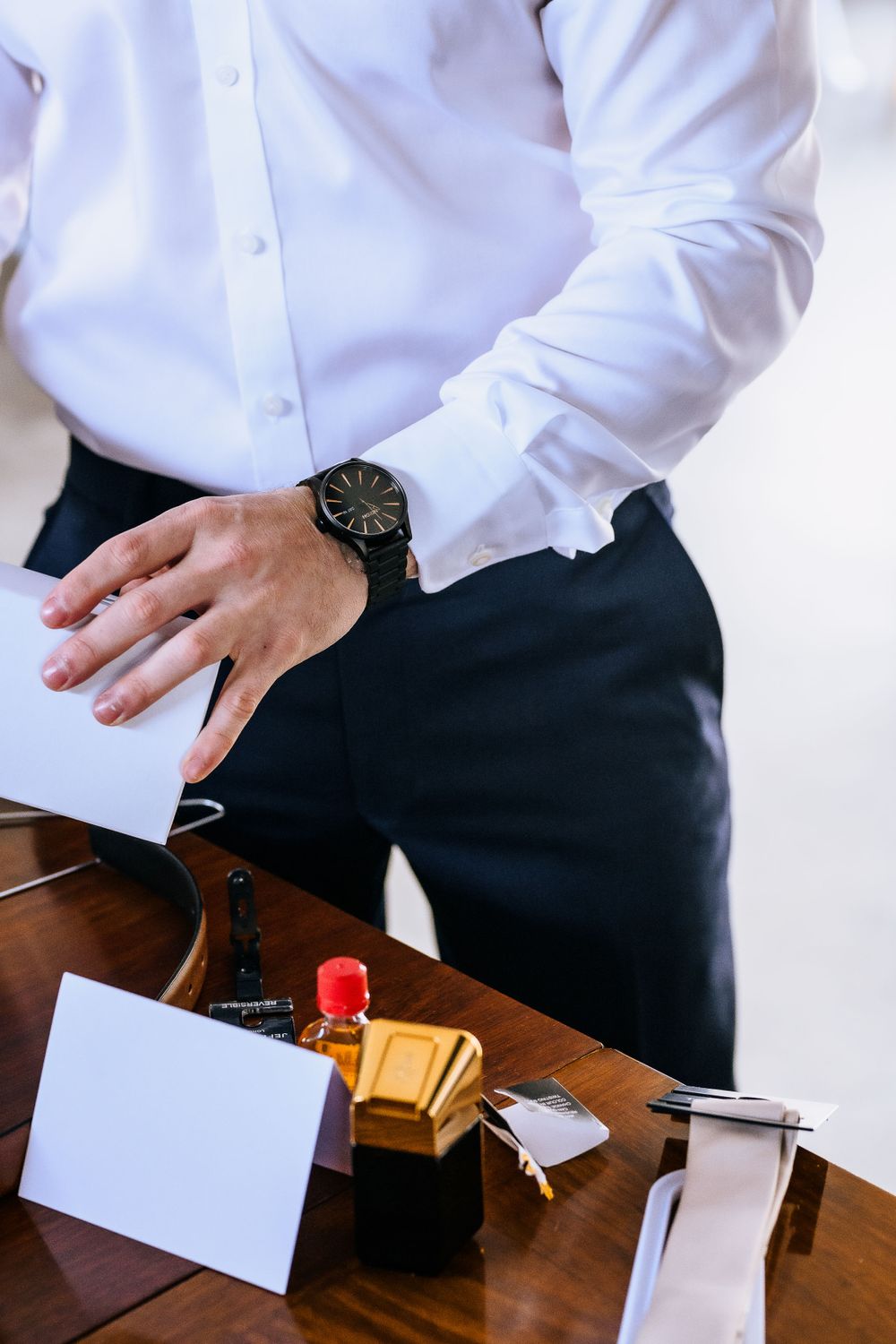Person wearing white dress shirt and watch checking papers on wooden desk with office supplies.