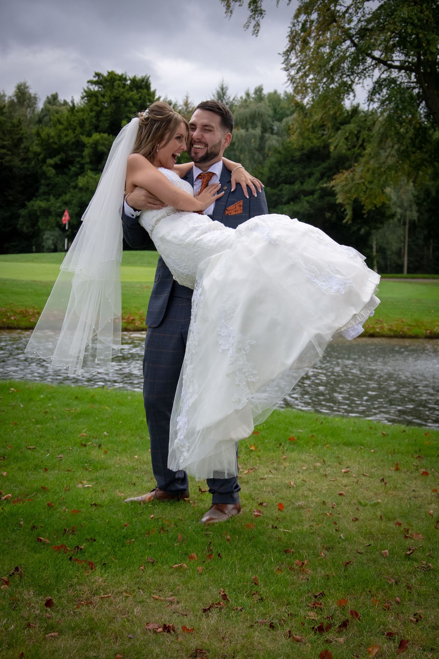 Romantic wedding pose by pond with couple in traditional formal attire.