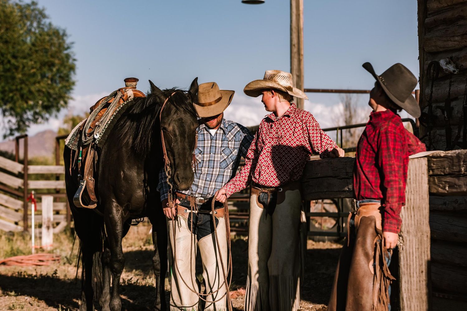 Group of cowboys gathered around a dark horse at a rustic ranch.