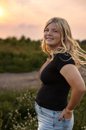 A person in jeans and black top poses outdoors during golden hour.