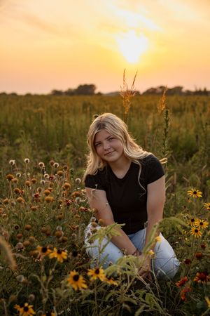 Person posing in a sunset wildflower field with sunflowers and tall grass during golden hour.