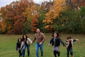 A group of people run playfully through a park with vibrant autumn foliage in the background.
