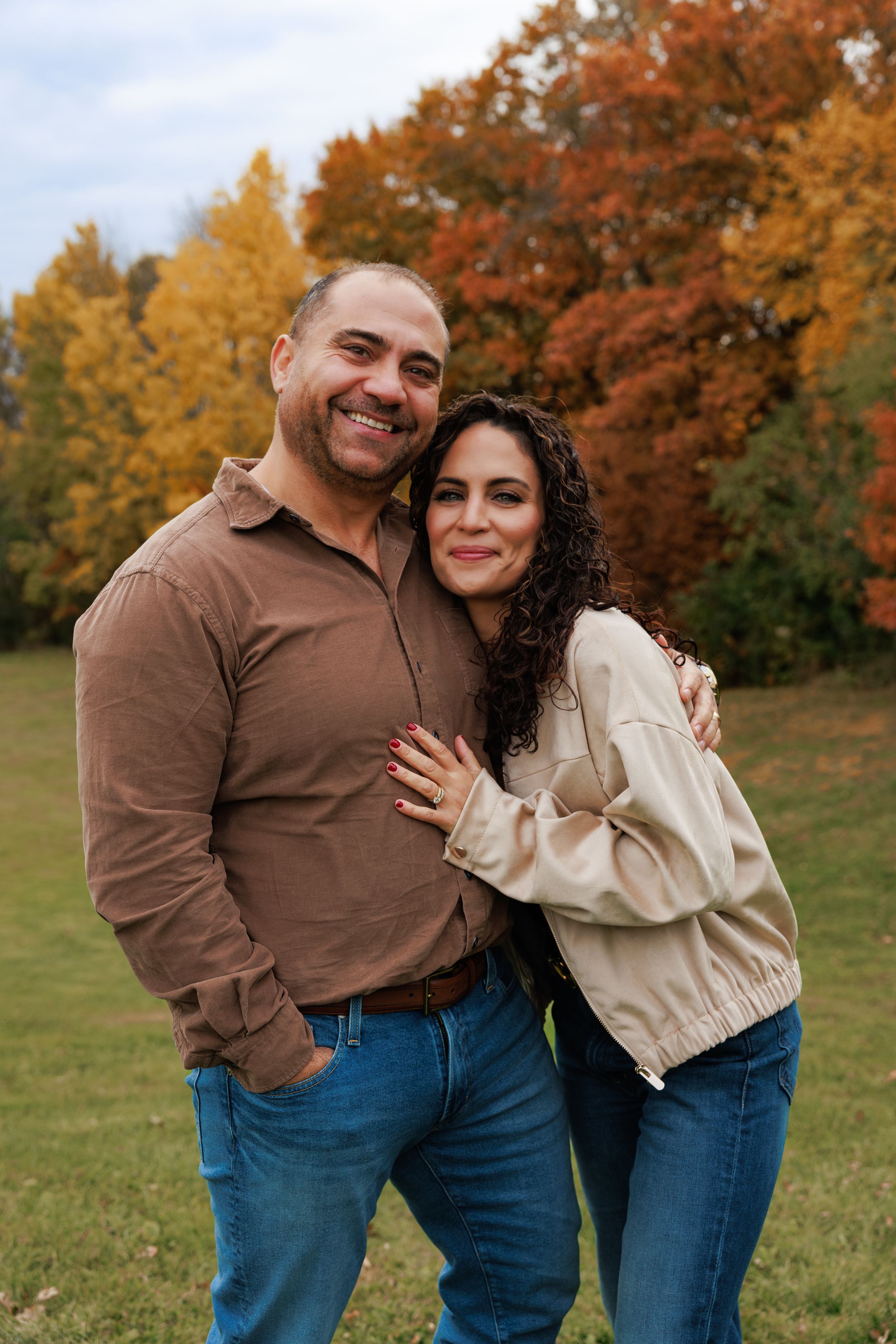 A couple shares a playful moment together outdoors with fall foliage in the background.