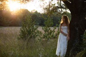 White dress silhouetted against golden sunset in a serene meadow.