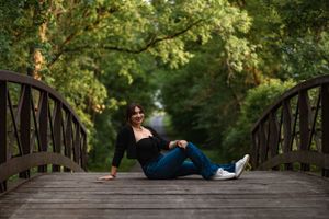 Figure lounging on a wooden bridge surrounded by lush green trees in a peaceful forest setting.