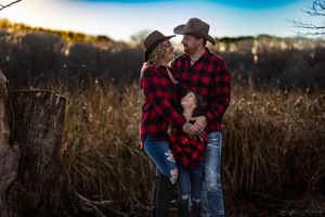 Couple in matching buffalo plaid shirts embrace in golden autumn field at sunset.