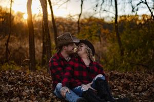 Couple in plaid shirts sharing intimate moment among fallen autumn leaves.