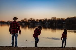 Three figures in plaid shirts cast silhouettes against a tranquil lakeside sunset.