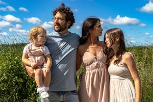 Family poses together in a sunny meadow filled with wildflowers on a bright summer day.