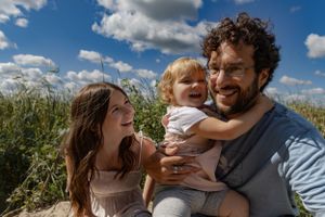 A joyful family moment outdoors with tall grass and puffy clouds in the background.