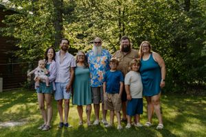 Group photo of family members wearing coordinated outfits standing on grass in front of trees.