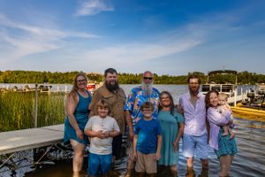 Family gathering on a wooden dock with boats and a lake in the background.