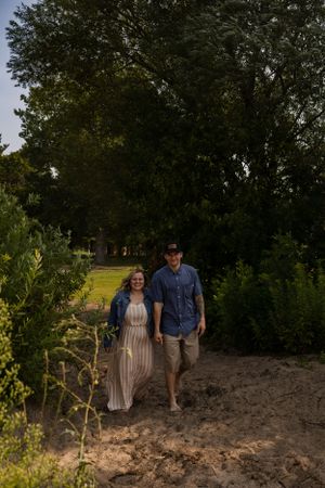 Couple walking together on sandy path surrounded by greenery at dusk.