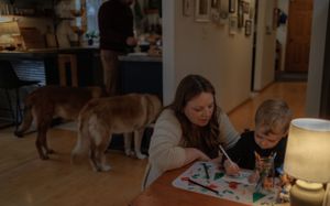 Parent and child doing arts and crafts together at home while a dog watches nearby.