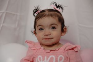 Baby wearing pink ruffled dress smiles against white background.